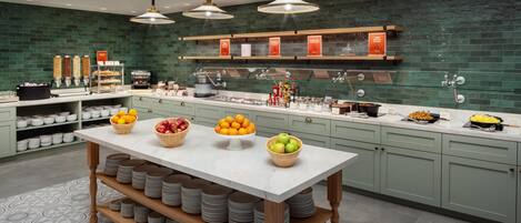 Una cocina moderna con encimera de mármol, una isla central con cuencos de fruta y un salpicadero con azulejos verdes.