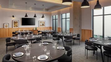 A conference room with multiple tables set for dining, large windows, and a flat-screen TV on the wall.
