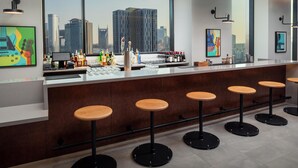 Uma área de bar com vista para a cidade, banquetas e diversos copos e garrafas.
