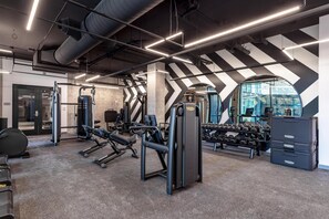 A modern gym with various exercise equipment, a large mirror, and a view of the city through a circular window.