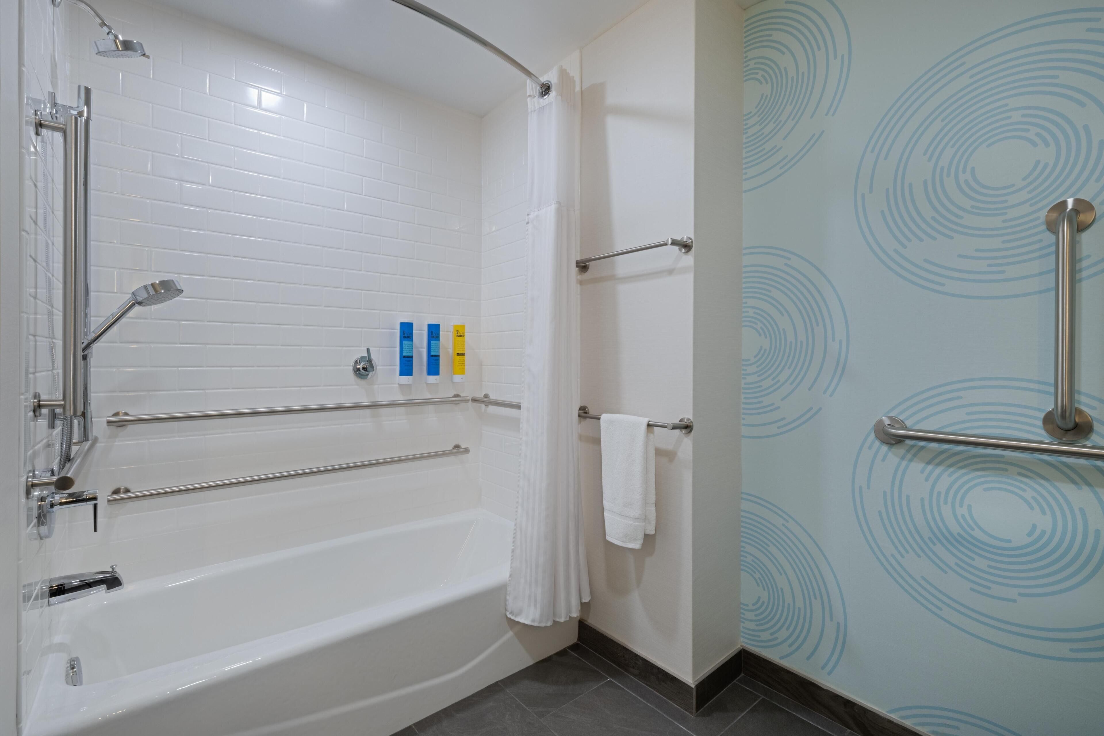 A modern bathroom with a white bathtub, grab bars, and a shower with a handheld showerhead.