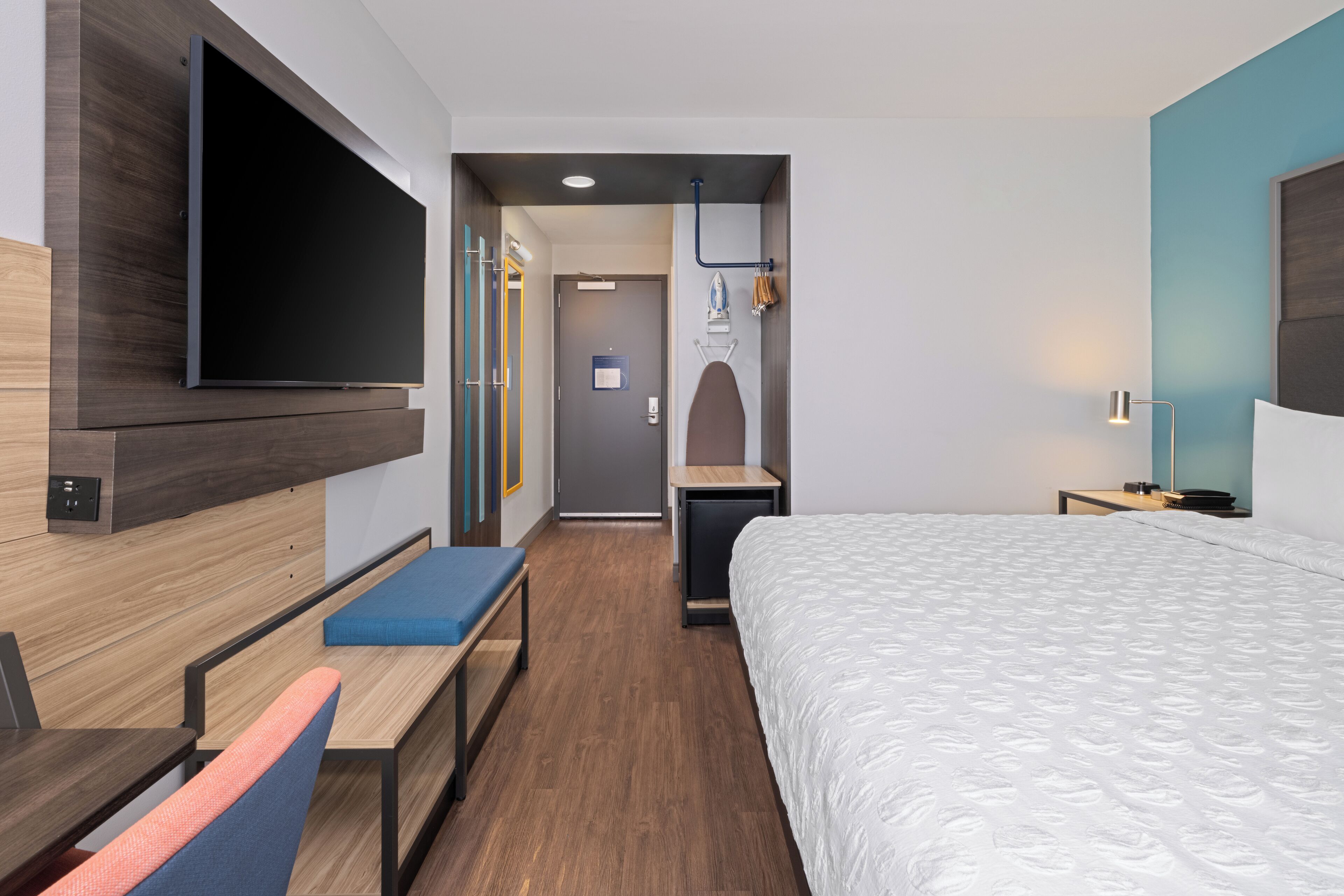 Ein modernes Hotelzimmer mit einem großen Bett, einem Flachbildfernseher an der Wand, einem Schreibtisch mit Stuhl und einer Bank.