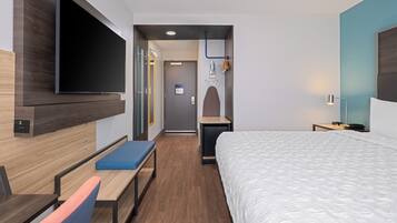 Ein modernes Hotelzimmer mit einem großen Bett, einem Flachbildfernseher an der Wand, einem Schreibtisch mit Stuhl und einer Bank.