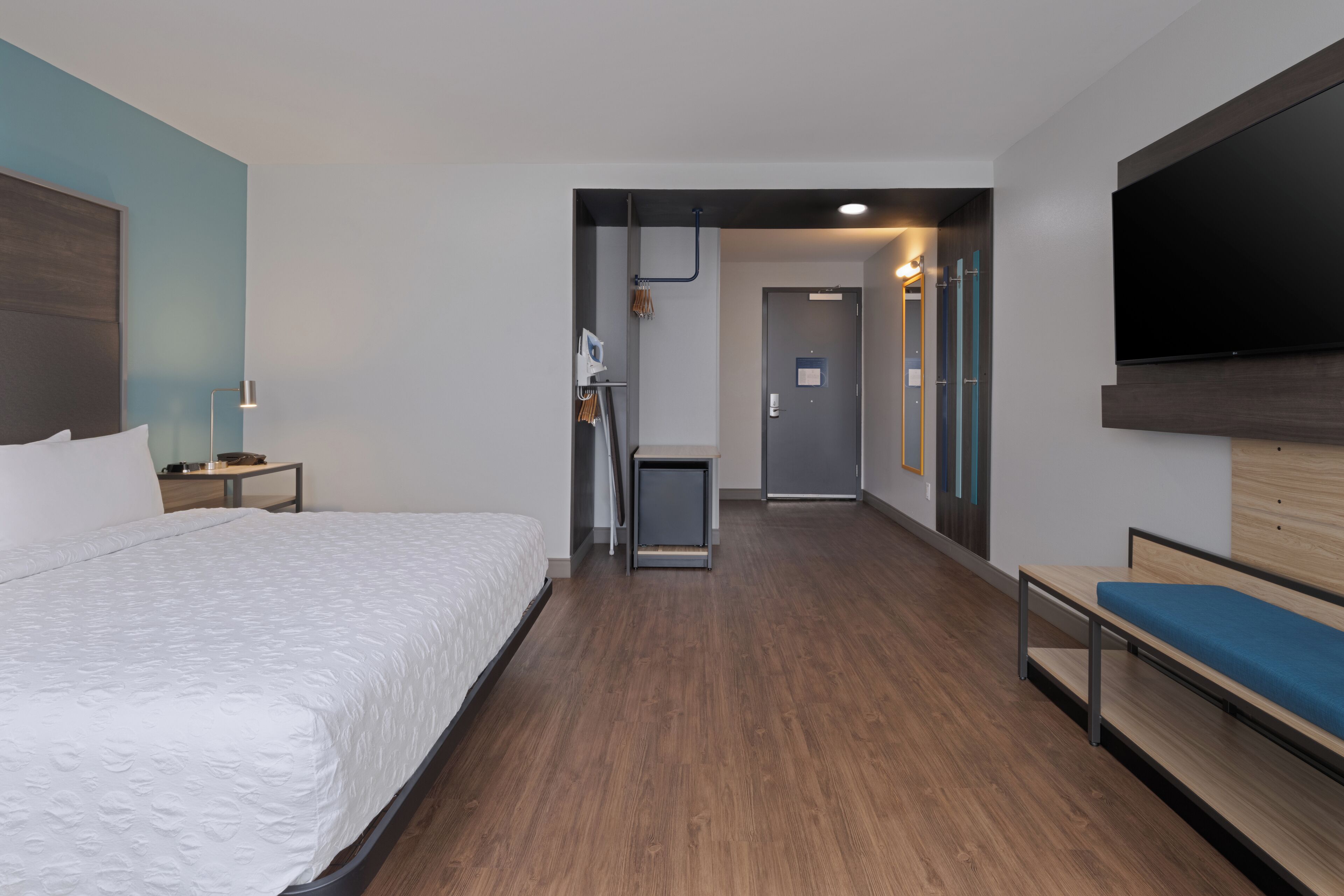 Habitación de hotel moderna con una cama grande, un escritorio, una silla, un televisor de pantalla plana y un banco de madera.
