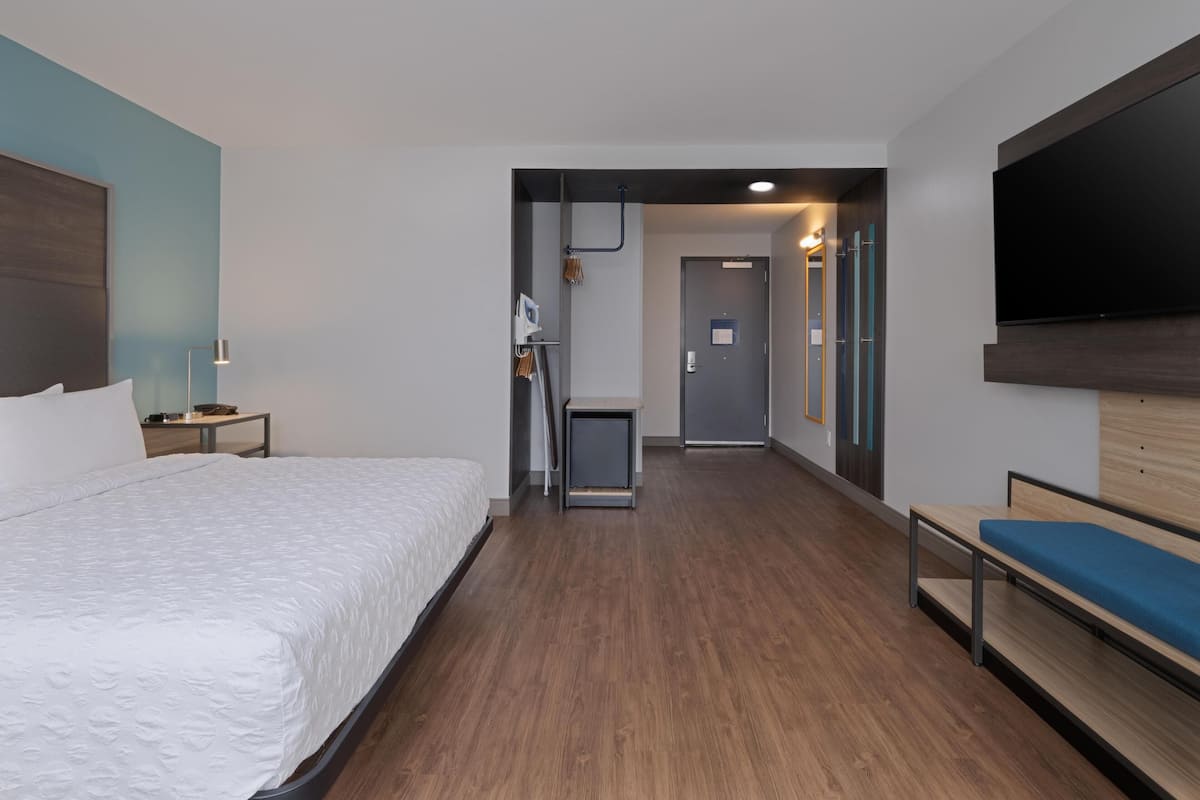 Une chambre d’hôtel moderne équipée d’un grand lit, d’un bureau, d’une chaise, d’une télévision et d’un couloir menant à la salle de bain.