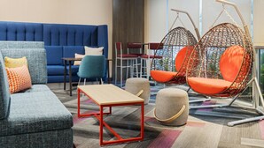 A modern lounge area with a blue sofa, a wooden table, and two hanging chairs. - Tru By Hilton Miramar (Miramar)