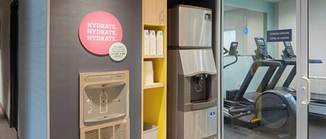 A hydration station with a water dispenser and reusable bottles, a fitness center with treadmills, and a sign indicating it's open 24 hours.