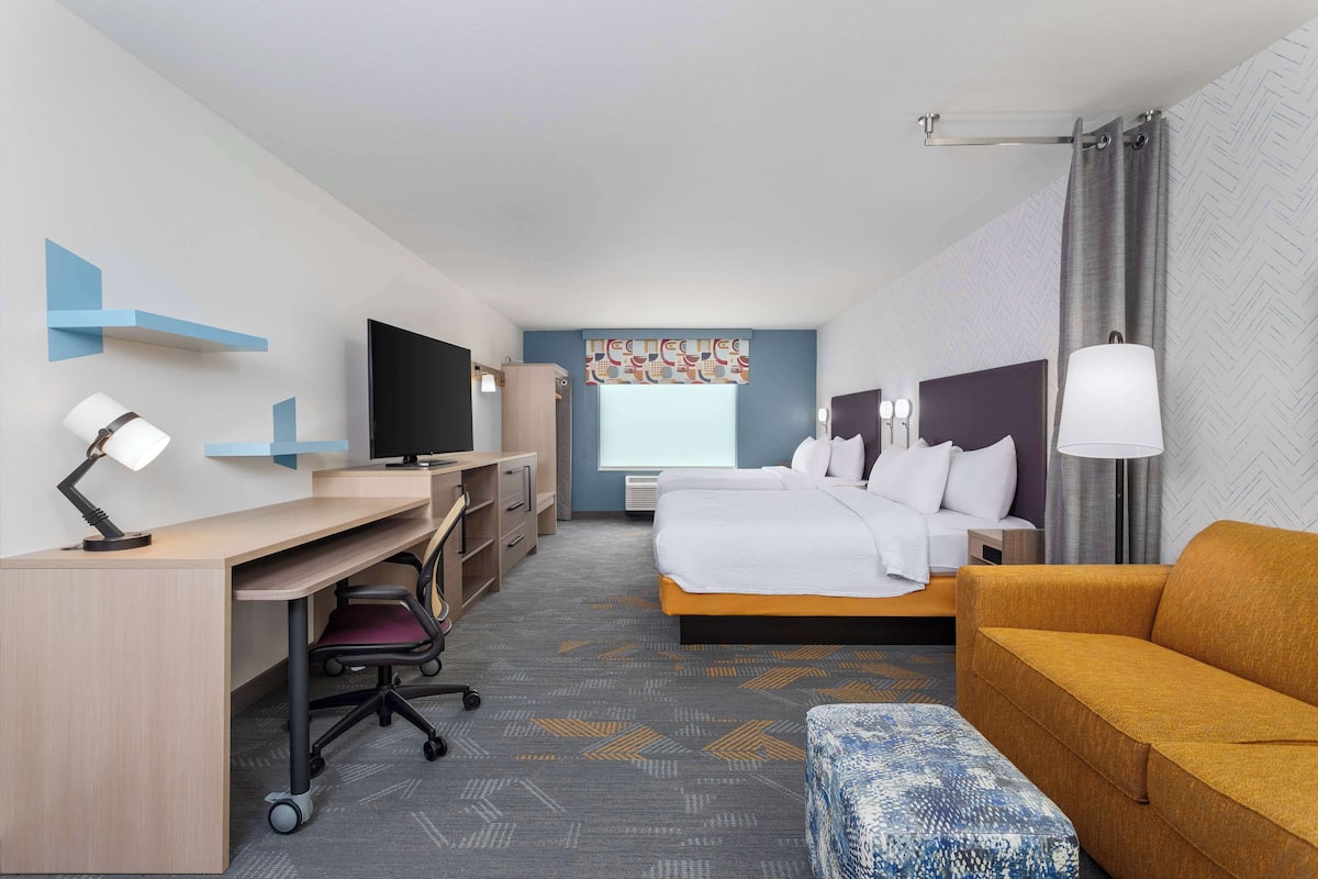 Une chambre d’hôtel comprenant un lit, un bureau avec une chaise, un canapé, une télévision et une fenêtre avec des rideaux.