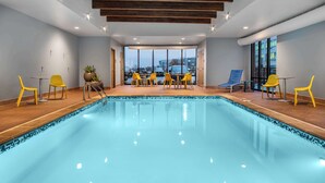 A modern indoor pool area with yellow chairs and a view of the city through large windows.