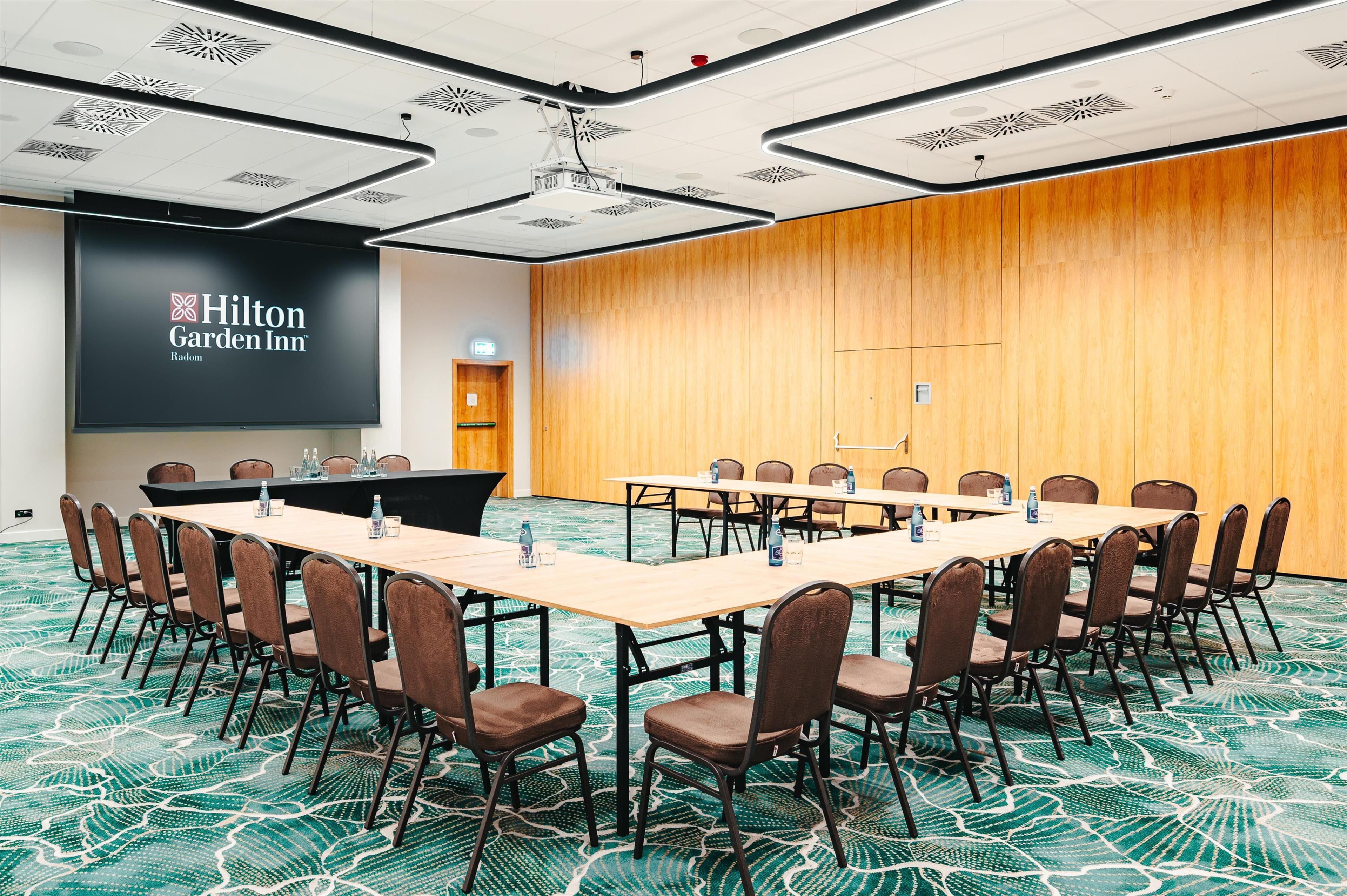 Un salón de conferencias con una larga mesa, sillas, una pantalla de proyector y un revestimiento de madera.