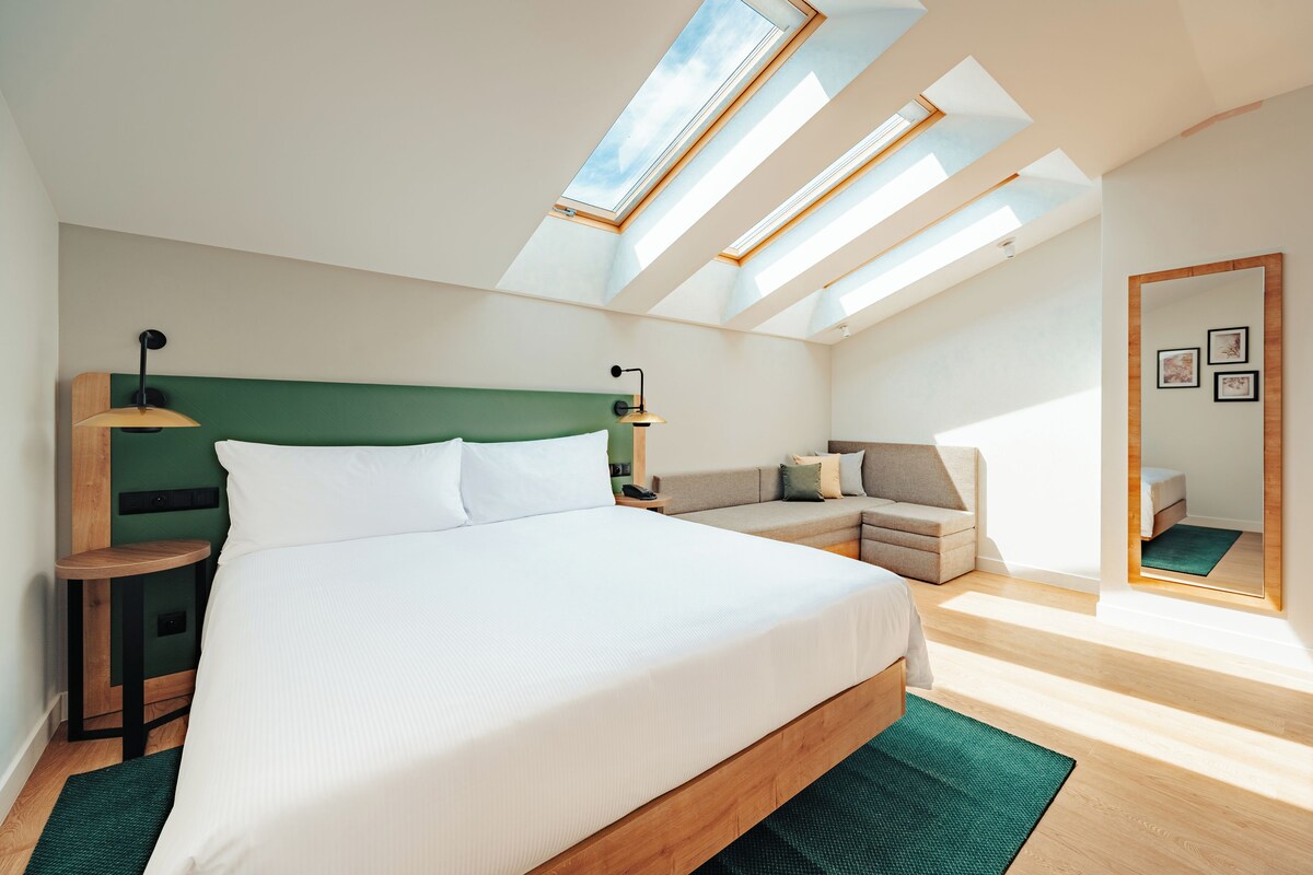 A modern bedroom with a large bed, a green headboard, and skylights.