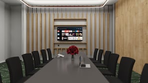 A conference room with a long table, black chairs, a floral centerpiece, and a mounted TV displaying streaming services. - Hilton Garden Inn Radom (Radom)