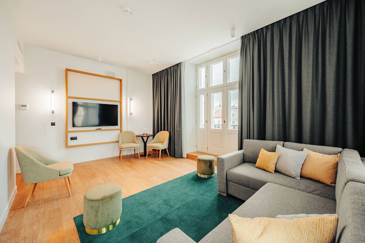 A modern living room with a grey sofa, a green armchair, a small round ottoman, and a TV mounted on the wall.