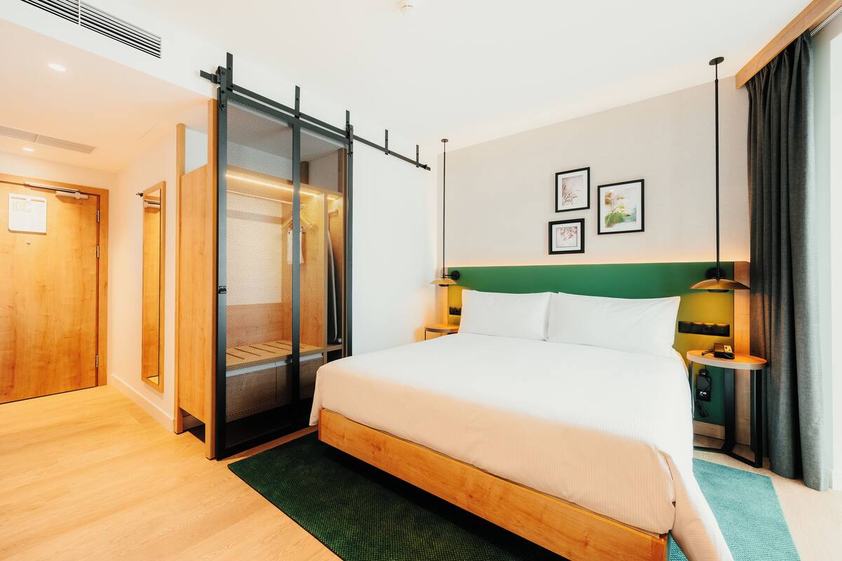 A hotel room with a bed, a sliding door closet, a bedside table with a lamp, and a green accent wall.