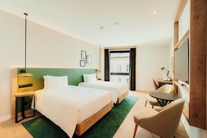 Une chambre d’hôtel avec deux lits, un bureau, une chaise, une télévision et une fenêtre donnant sur des immeubles.