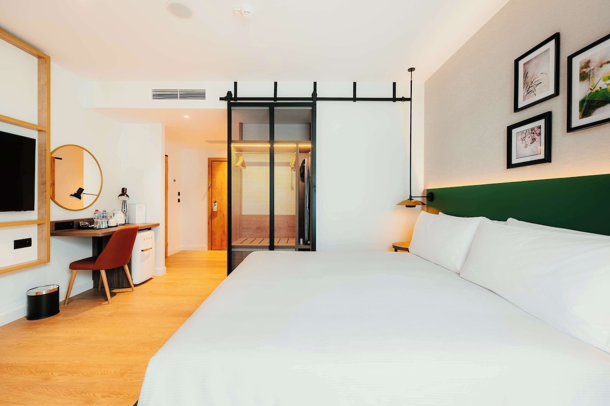 A hotel room with a bed, desk, chair, and a sliding door leading to a bathroom.