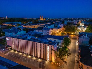 Un hôtel moderne doté d’une façade verticale imposante, d’un grand parking et offrant une vue sur le paysage urbain environnant au crépuscule.