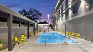 A modern hotel pool area with a rectangular pool, yellow chairs, and blue lounge chairs. - Home2 Suites By Hilton Niceville Eglin Air Force Base (Niceville)