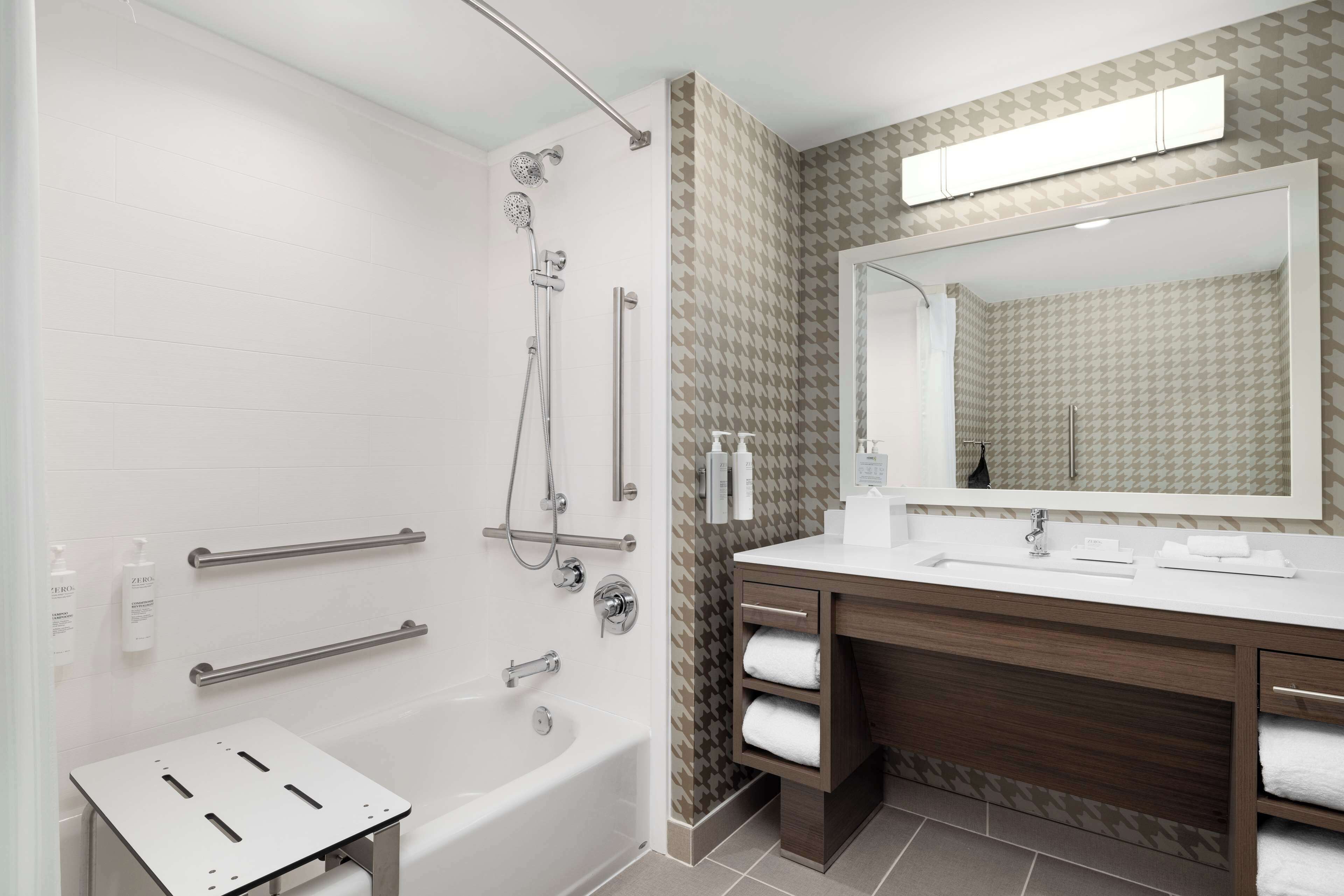 A modern bathroom with a walk-in shower, grab bars, a vanity with a mirror, and a bathtub.