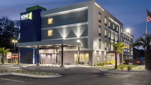 A modern hotel with a covered entrance, multiple floors, and a flag. - Home2 Suites By Hilton Niceville Eglin Air Force Base (Niceville)