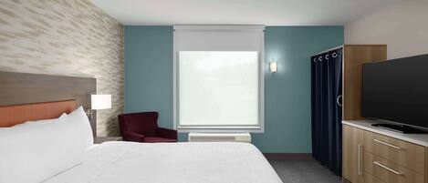 A hotel room with a bed, a TV, a desk, and a window with curtains.