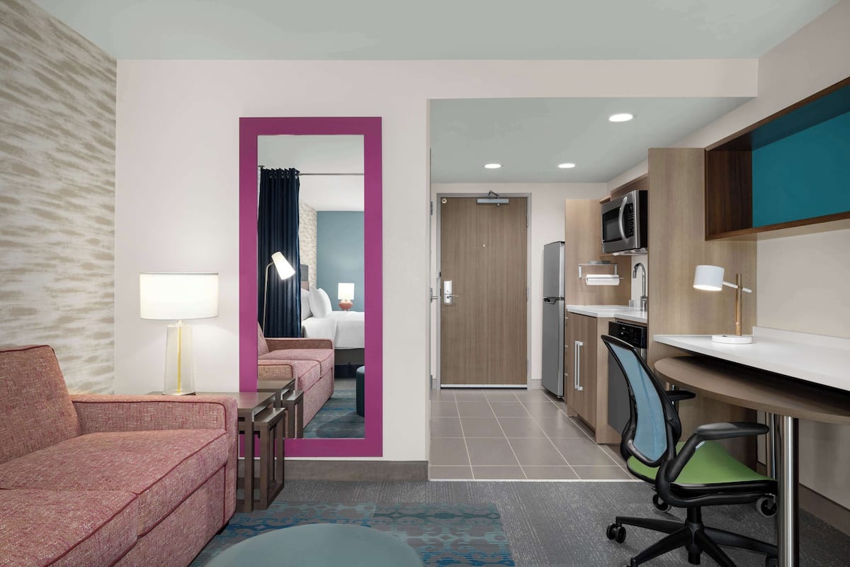 Ein modernes Hotelzimmer mit Sofa, Schreibtisch und Küchenzeile.
