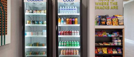Two refrigerated display cases labeled "COLDER" containing beverages and snacks, with a sign stating "HOME IS WHERE THE SNACKS ARE".