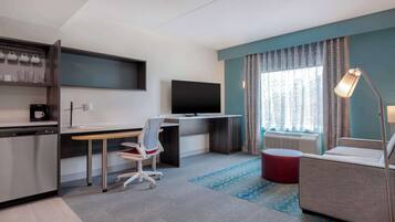 A modern hotel room with a desk, television, and seating area.