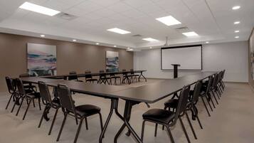 A conference room with a long table, chairs, a projector screen, and two large paintings on the walls.
