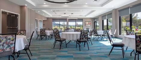 Une pièce spacieuse avec des tables et des chaises rondes, de grandes fenêtres offrant une belle vue et un tapis à motifs.