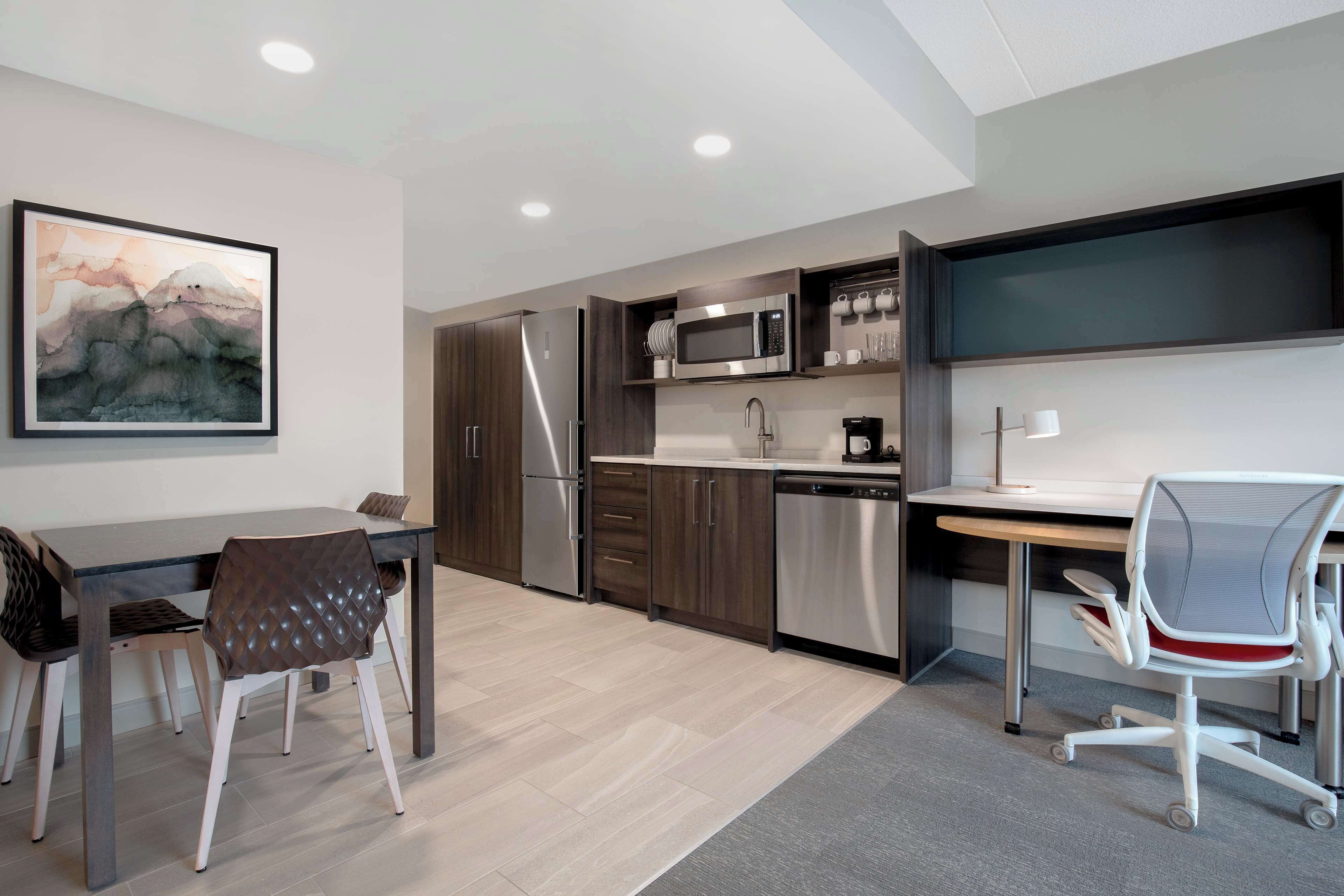 A modern kitchen with a dining area, including a table, chairs, and a painting on the wall.
