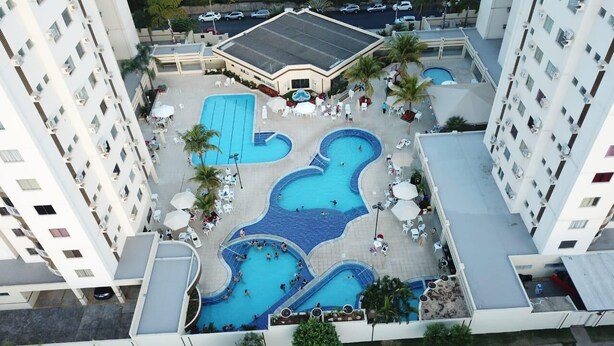 Ein Poolkomplex auf einem Dach, umgeben von Hochhäusern, mit mehreren Pools und Liegebereichen.