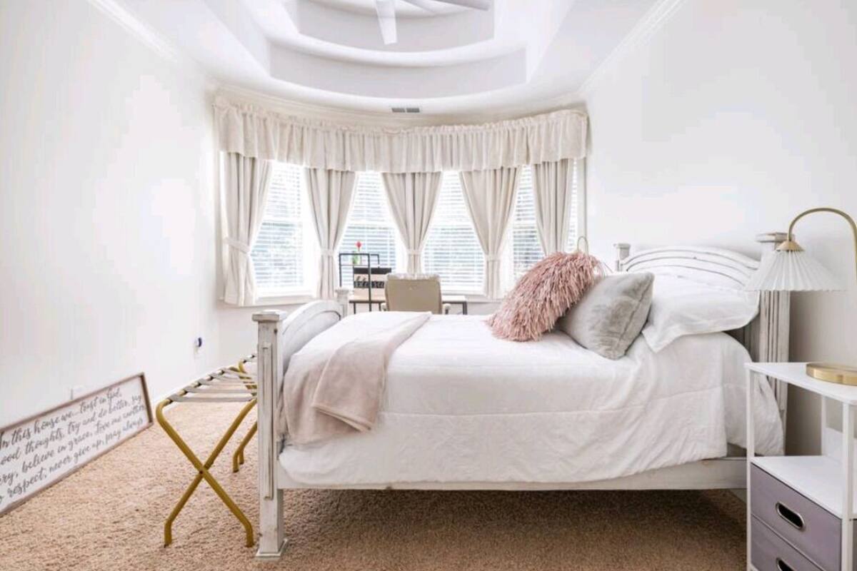 A bedroom with a bed, bedside table, lamp, and a window with curtains.