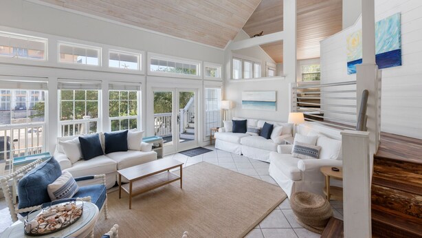 A spacious living room with a high ceiling, large windows, and a staircase leading to an upper level. - Vast Luxurious Home in Gated Community + Pool (Seacrest)
