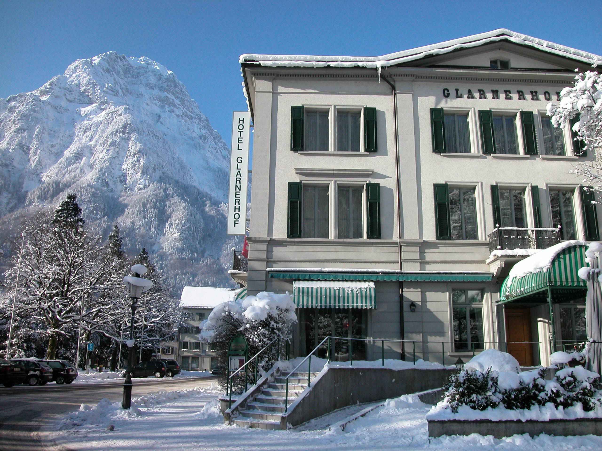 Ein Hotel mit einem Schild, auf dem 'GLARNERHOF HOTEL' steht, vor einer Berglandschaft.
