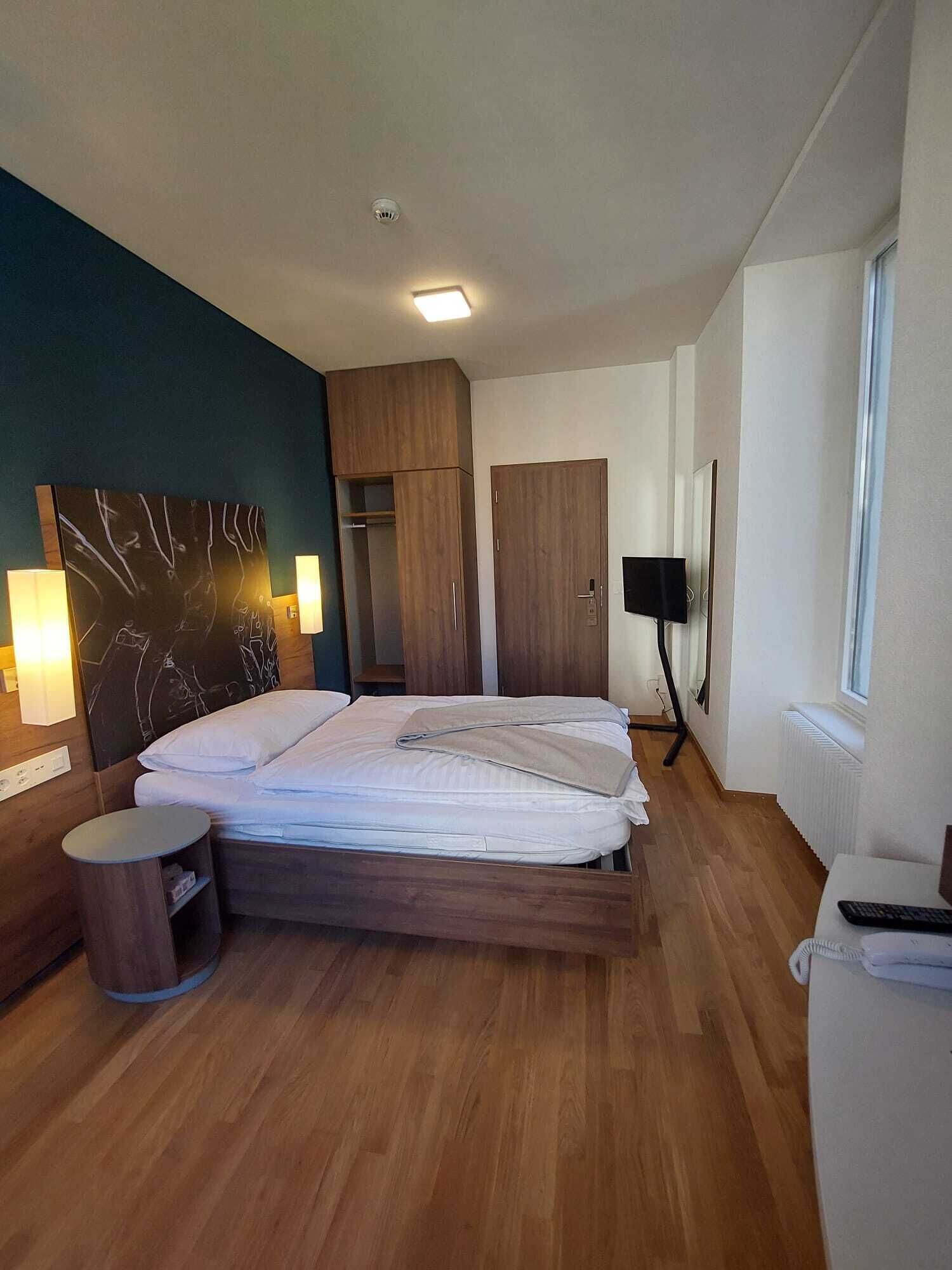 Un dormitorio moderno con una cama de madera, mesitas de noche, un armario y un espejo grande.