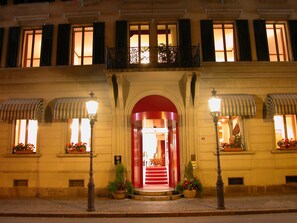 Un edificio histórico con entrada roja, ventanas grandes con contraventanas e iluminación exterior.
