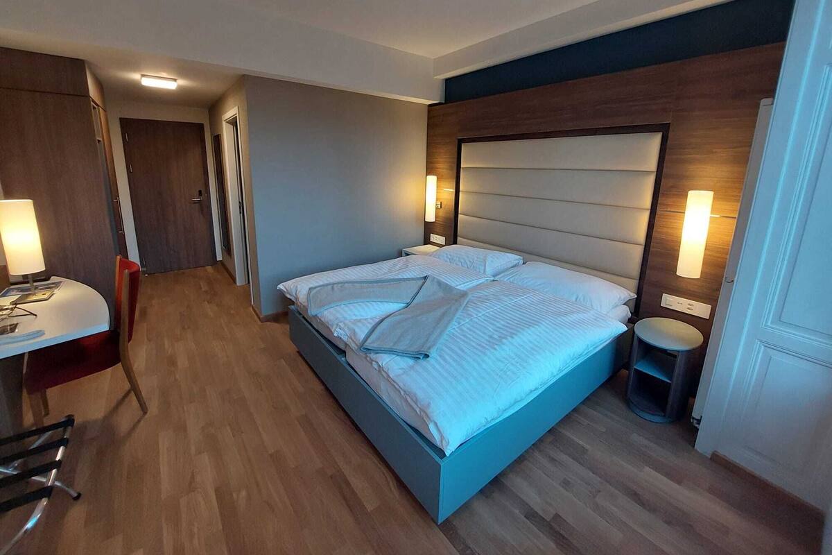 A modern hotel room with a large bed, bedside tables, a desk, and a chair.