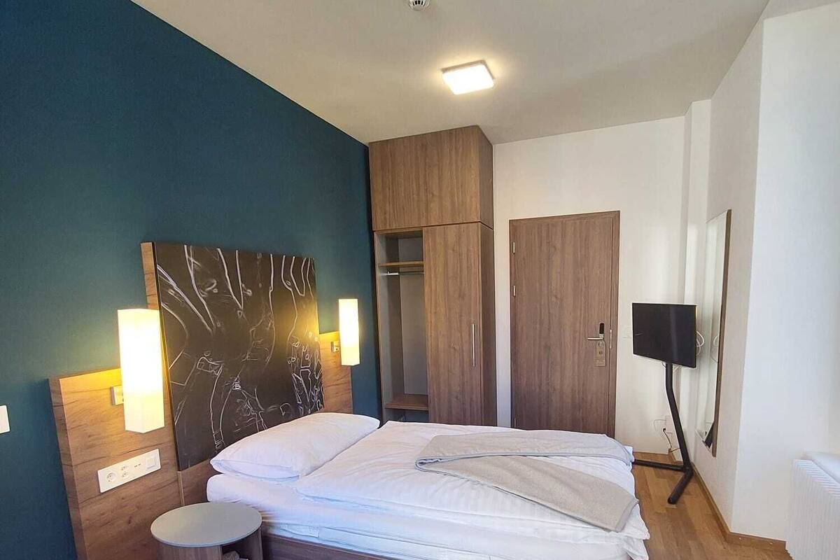 A modern bedroom with a wooden bed, a bedside table, a wardrobe, and a flat-screen TV mounted on the wall.