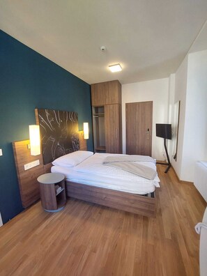 Un dormitorio moderno con una cama de madera, una mesita de noche, un armario y un televisor de pantalla plana montado en la pared.
