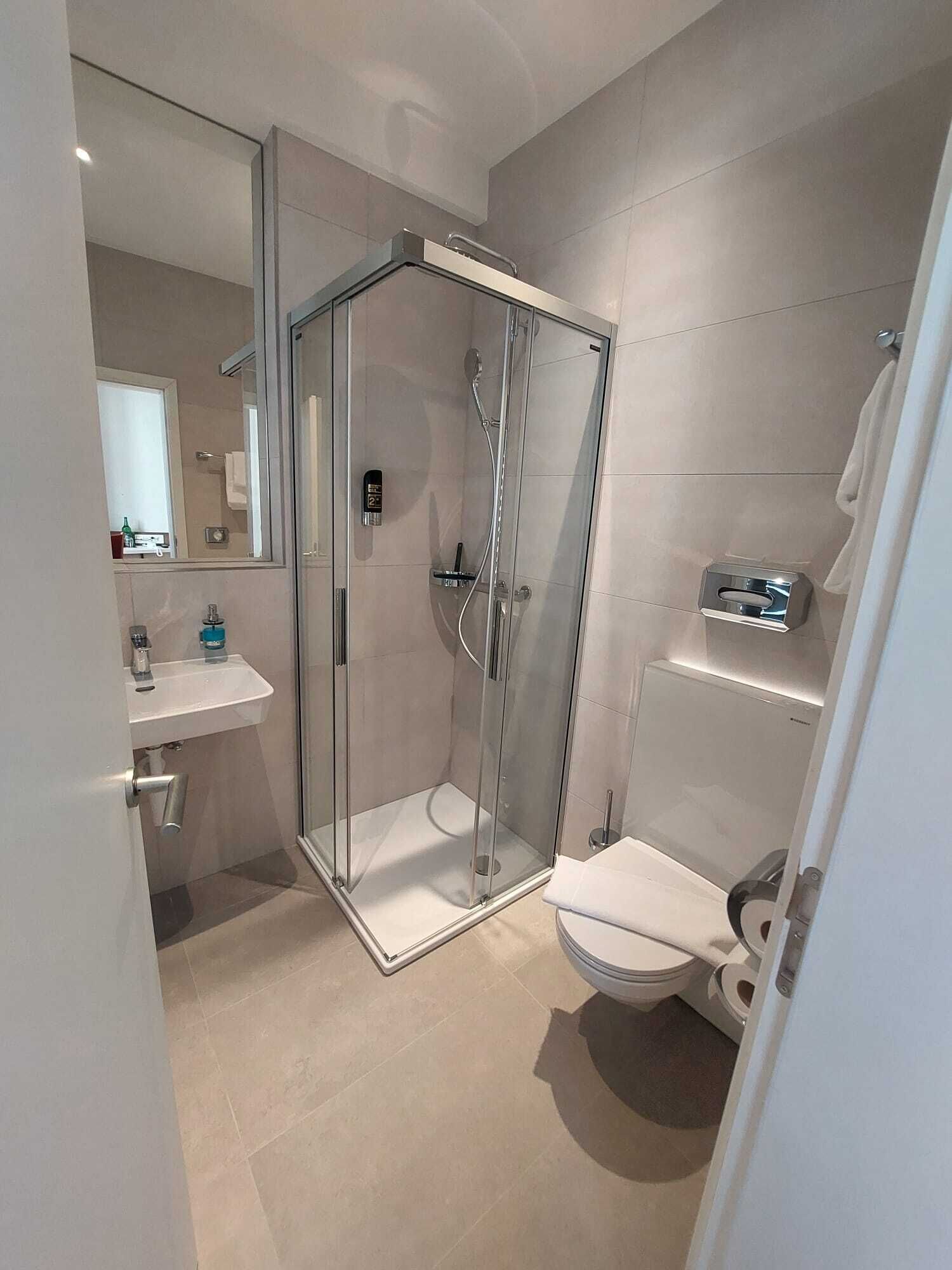 Un baño moderno con ducha de vidrio, lavamanos blanco y retrete.