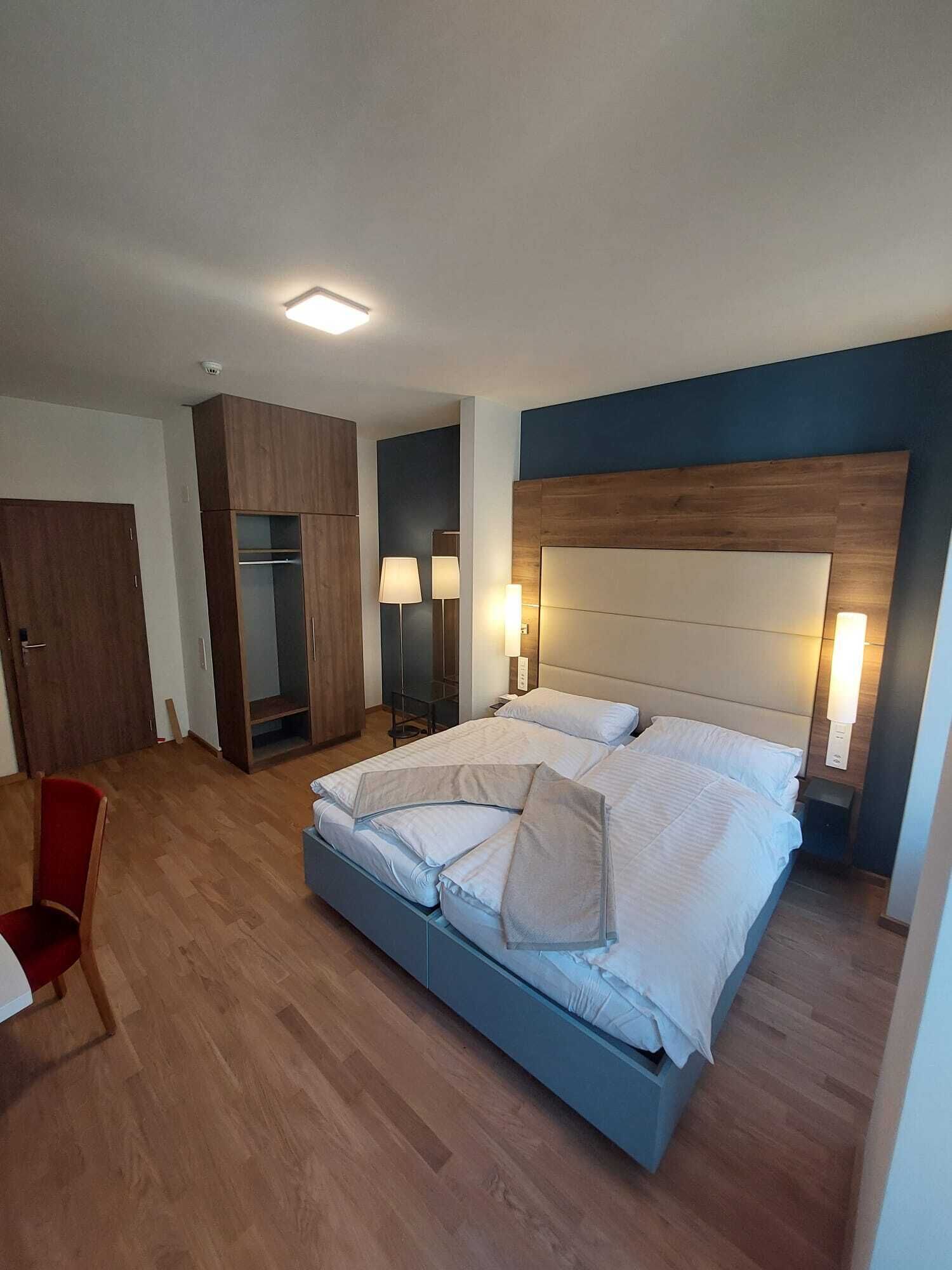 A modern bedroom with a large bed, wooden wardrobe, and a red chair.