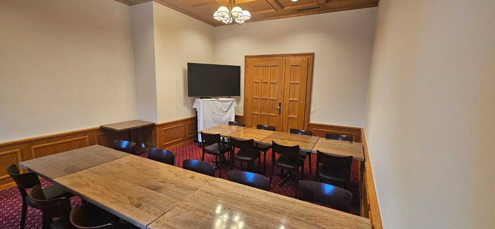 A conference room with a large table, multiple chairs, a television, and a wooden door.