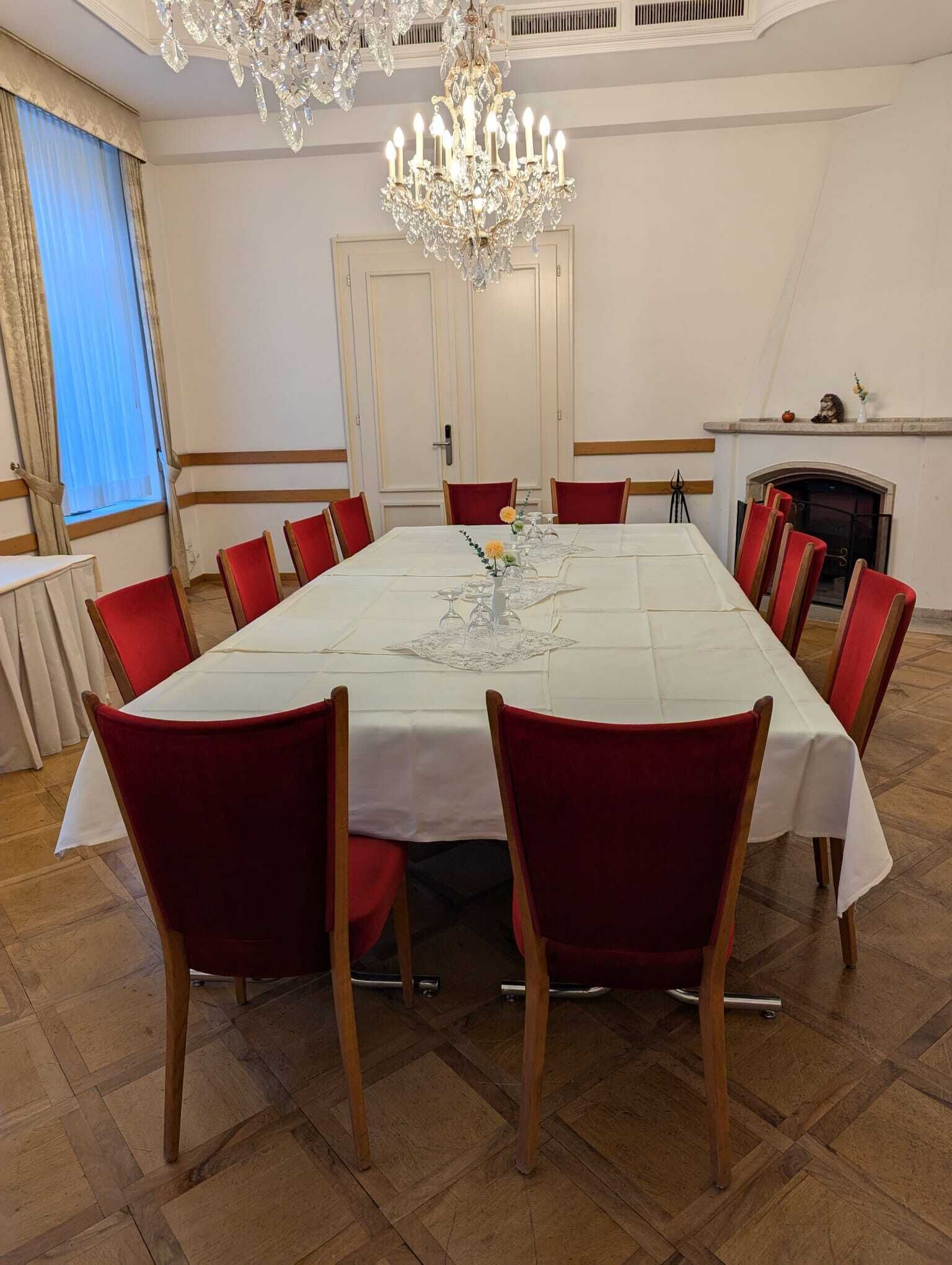 Ein formeller Essraum mit einem großen rechteckigen Tisch, roten Polsterstühlen, einer Kronleuchter und einem Kamin.