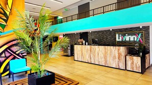 Un hall d’hôtel moderne avec un comptoir d’accueil, un fauteuil bleu et une grande plante en pot.