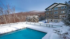 Ein Hotel mit Pool, umgeben von verschneiter Landschaft und Bergen im Hintergrund.