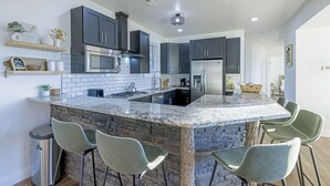 A modern kitchen with dark cabinets, a central island with bar stools, a stainless steel refrigerator, and a microwave.