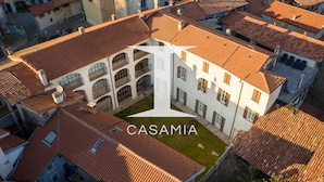 An aerial view of a building with a courtyard, surrounded by other buildings with red-tiled roofs. - PM6        (Castello Cabiaglio)