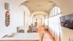 A spacious living area with a dining table, chairs, a sofa, and a TV mounted on the wall. - PM6        (Castello Cabiaglio)
