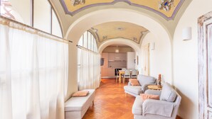 A spacious living area with a sofa, a bench, and a dining table. A kitchen is visible in the background. - PM6        (Castello Cabiaglio)